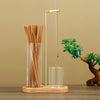 A glass incense holder with bamboo sticks and a metal rod is displayed next to a small green plant.