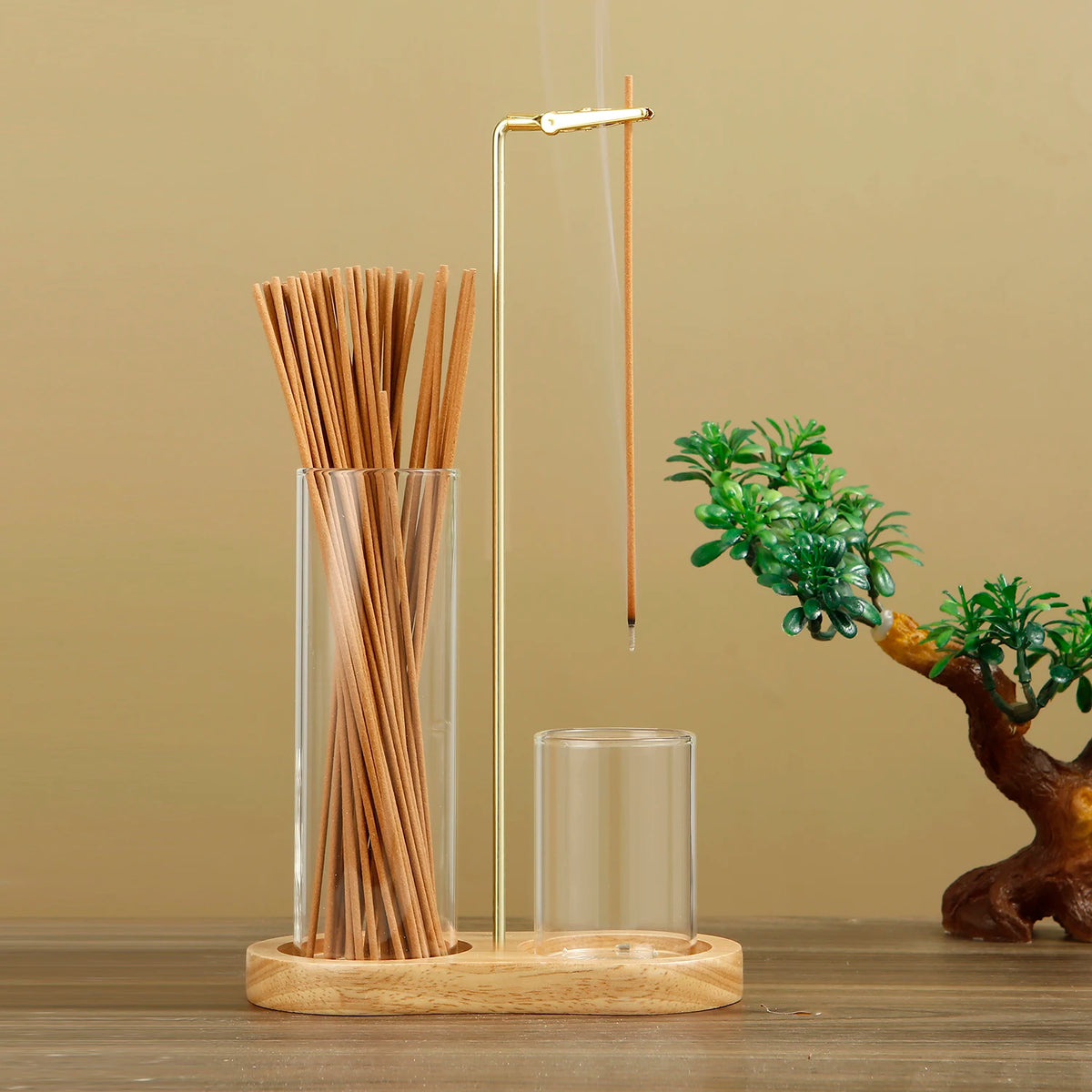 A glass incense holder with bamboo sticks and a metal rod is displayed next to a small green plant.