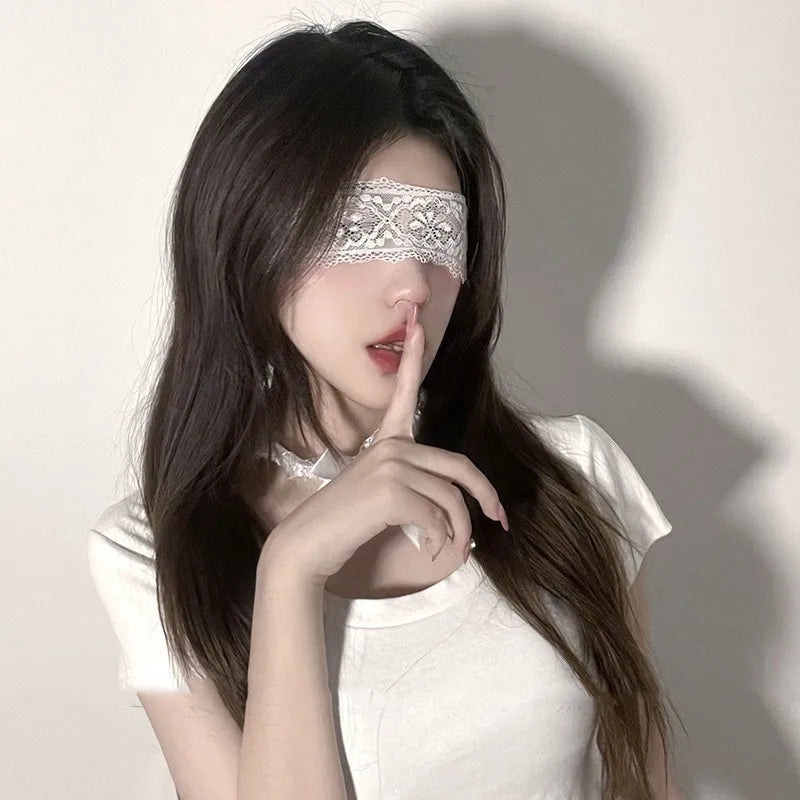 A woman with long dark hair wearing an elegant lace masquerade eye mask and touching her lips.