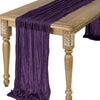 A deep purple semi-sheer gauze table runner draped over a wooden table.