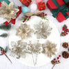 A white plate displays artificial silver and gold floral arrangements and red wrapped gifts on a white fluffy surface.