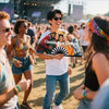 A smiling man holds a custom photo and name folding fan while walking through an outdoor event.