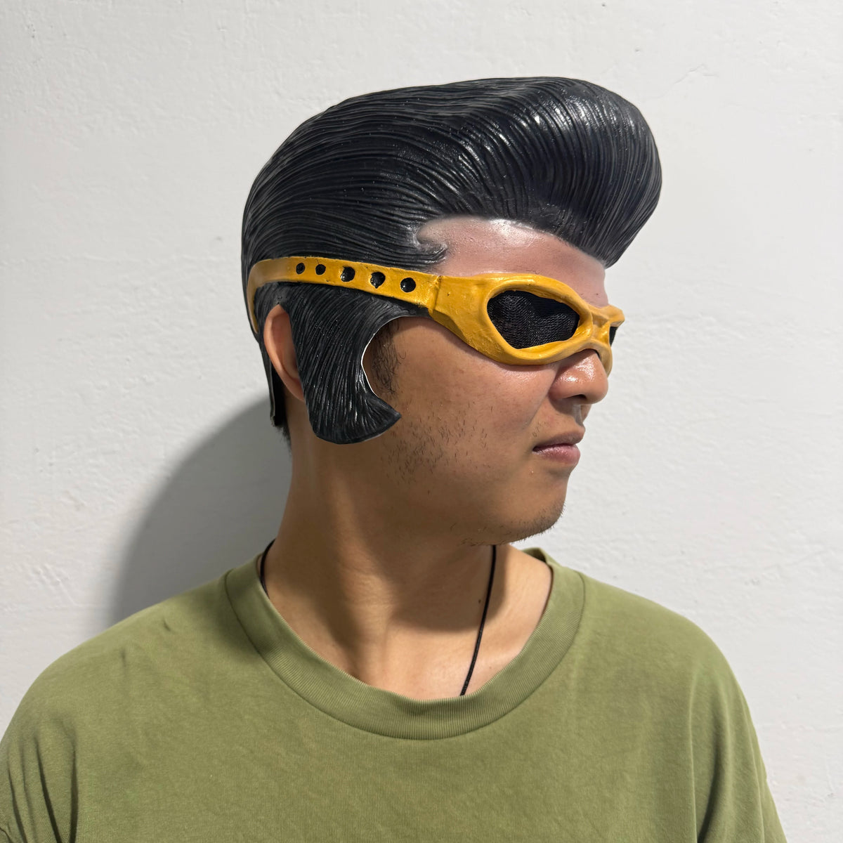 A man wearing a yellow latex half-face mask with black hair and a green shirt.