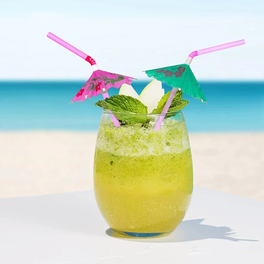 A yellow citrus drink garnished with mint leaves and decorated with pink and green paper umbrellas on a white surface.