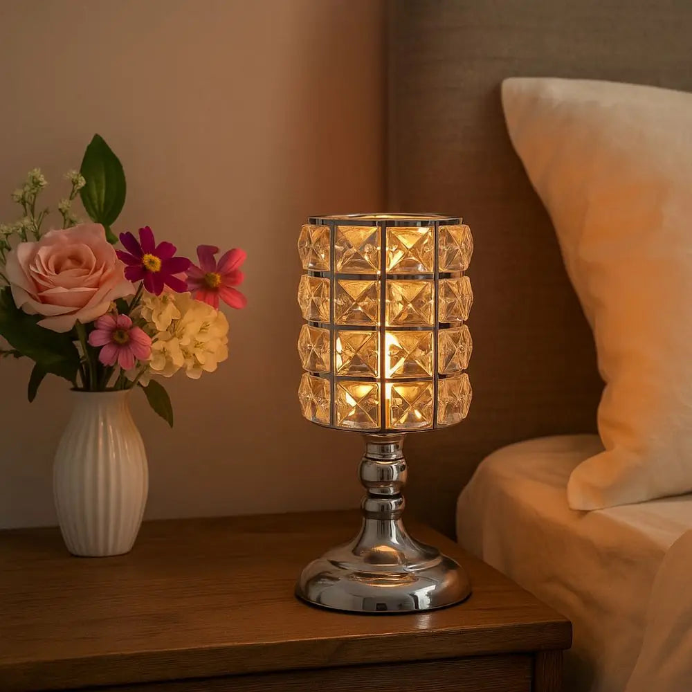 Un portavelas de cristal plateado con un brillo cálido sobre una mesa de madera junto a un arreglo de rosas rosas.