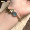 A macrame bracelet featuring a rose accent and a blue aquamarine bead worn on a hand.