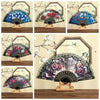 A collection of Spanish style folding lace trim handheld fans in various colors and patterns displayed on a wooden surface.