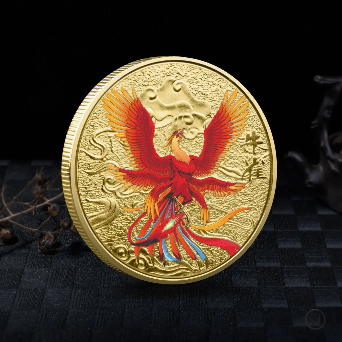 A gold collectible coin featuring a red mythical bird with outstretched wings and a Tai Chi motif.