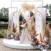 A wedding backdrop featuring gold metal arches decorated with dried floral arrangements and greenery.