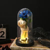 An eternal rose LED decorative flower with a blue rose inside a glass dome and a teddy bear figure.