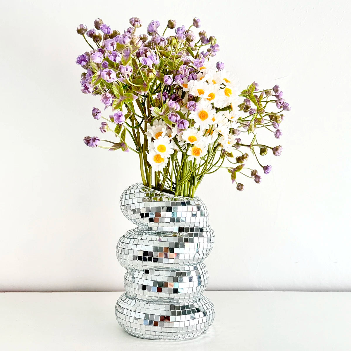 A bouquet of purple and white flowers displayed in a stack of silver mirror tile disco ball vases.