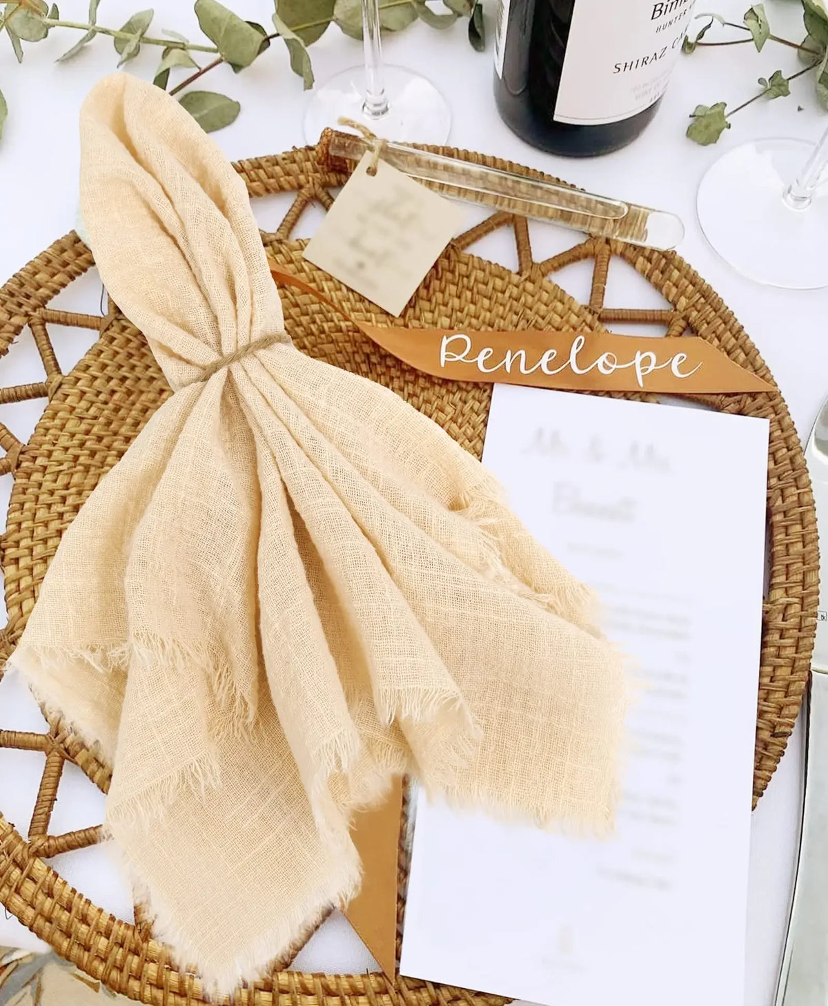 A light beige handcrafted cotton napkin tied into a bow resting on a woven placemat with a menu card.