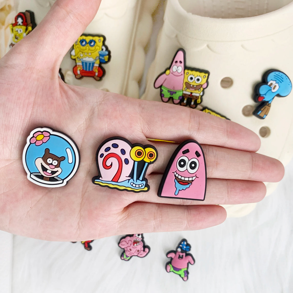 A hand holds a set of SpongeBob SquarePants shoe charms featuring characters like Patrick and Squidward.