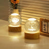 A glowing crystal ball night light with a white deer silhouette on a wooden base.