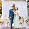 A couple stands in front of an elegant white rectangular backdrop drape for an event.