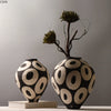 A hand-drawn ceramic vase with a black and white geometric circle design, featuring dry branches.