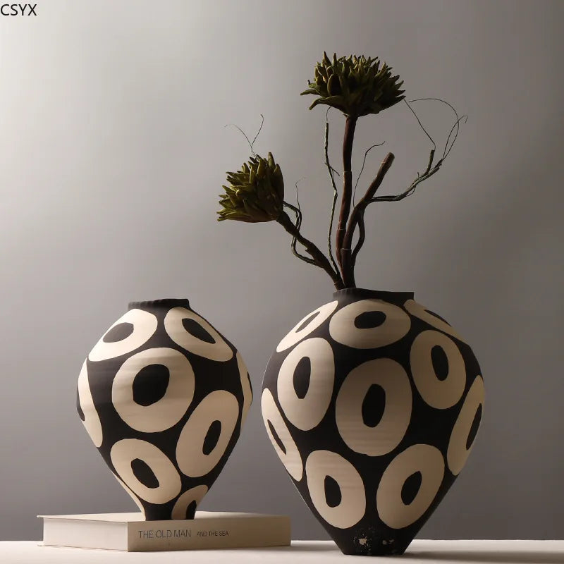 A hand-drawn ceramic vase with a black and white geometric circle design, featuring dry branches.
