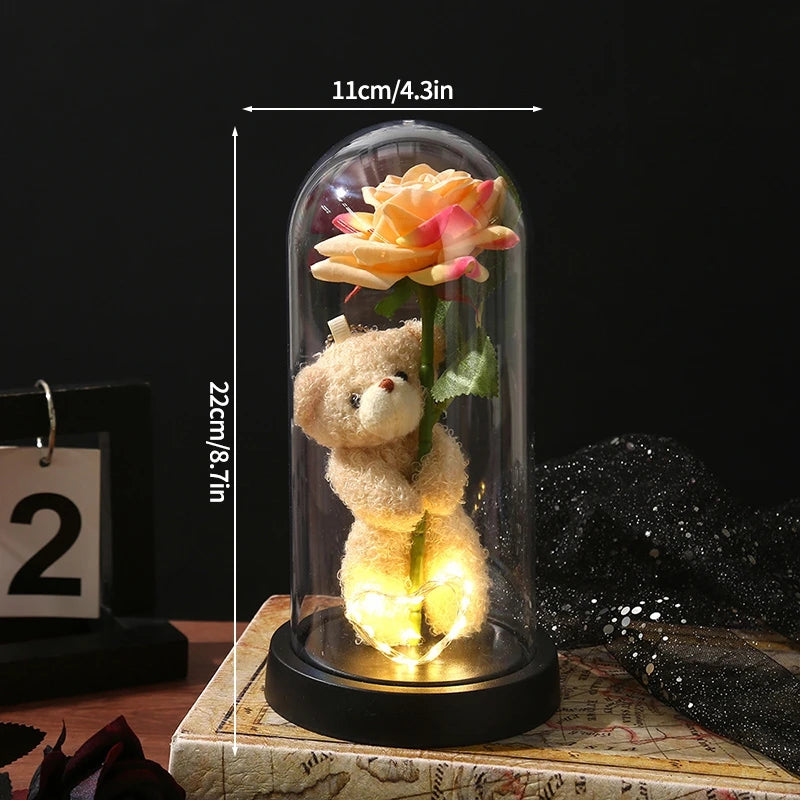 A glass dome display featuring an eternal rose and a small teddy bear.