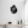 A black vinyl record wall clock shaped like the Millennium Falcon, mounted on a white wall above a wooden table.