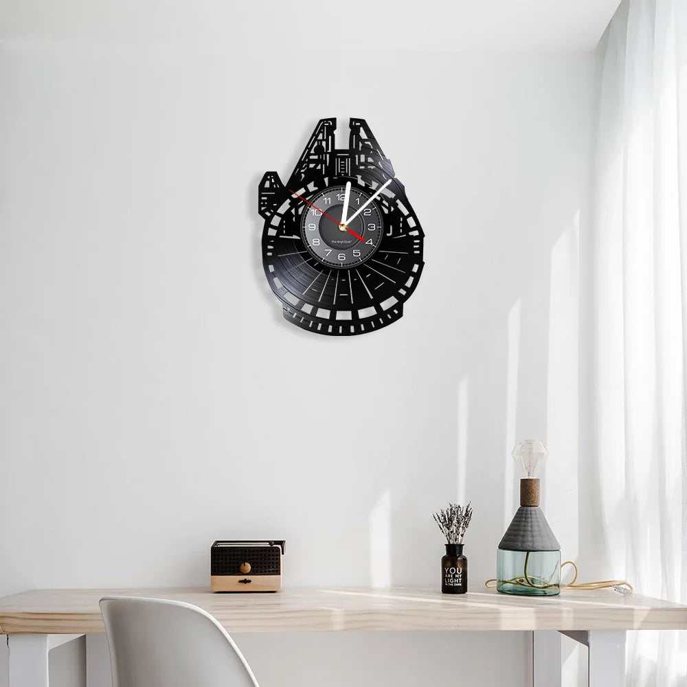 A black vinyl record wall clock shaped like the Millennium Falcon, mounted on a white wall above a wooden table.