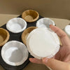 A hand holds a white fluted paper cup, surrounded by several natural brown fluted cups.