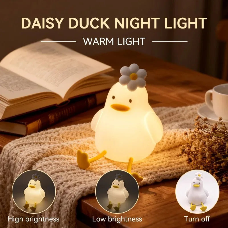 A glowing white duck night light is shown resting on a knitted fabric next to a book and dried flowers.