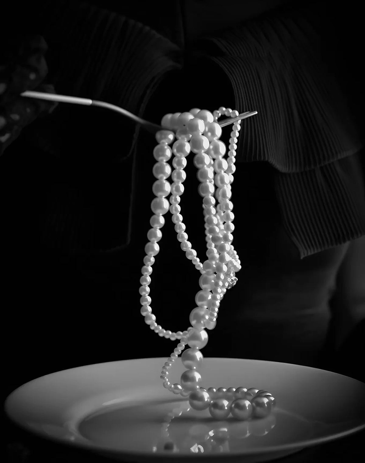 A delicate strand of white pearls rests on a white plate against a dark background.