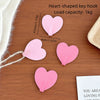 A set of pink heart-shaped key hooks with no-drill adhesive backing displayed on a wooden surface.