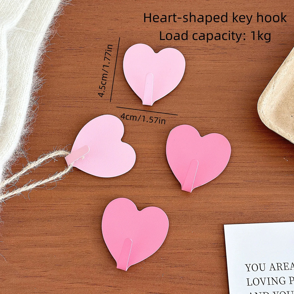A set of pink heart-shaped key hooks with no-drill adhesive backing displayed on a wooden surface.