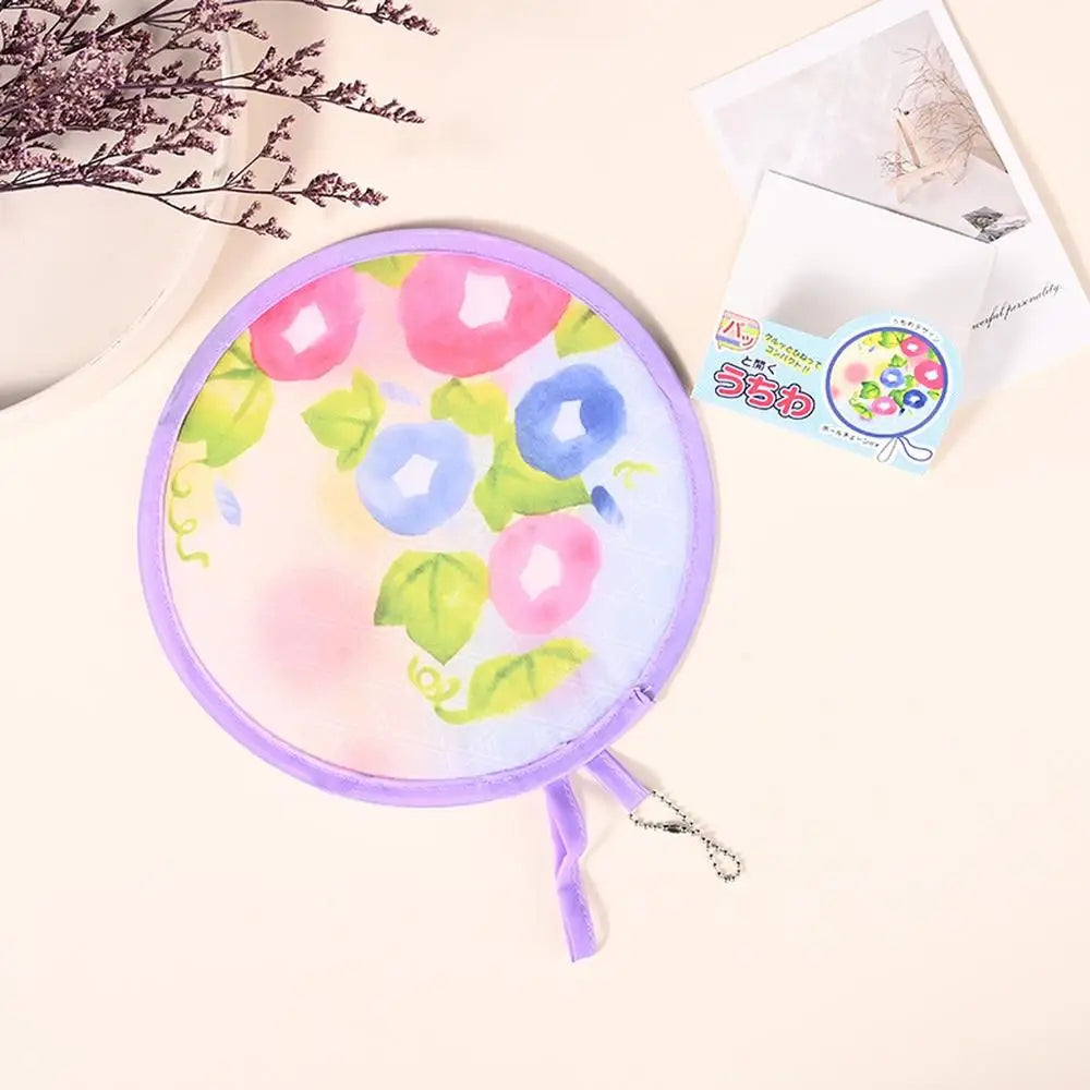 A purple fabric fan with colorful floral designs is shown next to a small card on a light background.
