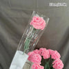 A clear glass vase holds a single pink crochet tulip flower with green stem and leaves.