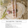 Two long-stemmed printed candles in light pink and green floral patterns displayed on a lace plate.