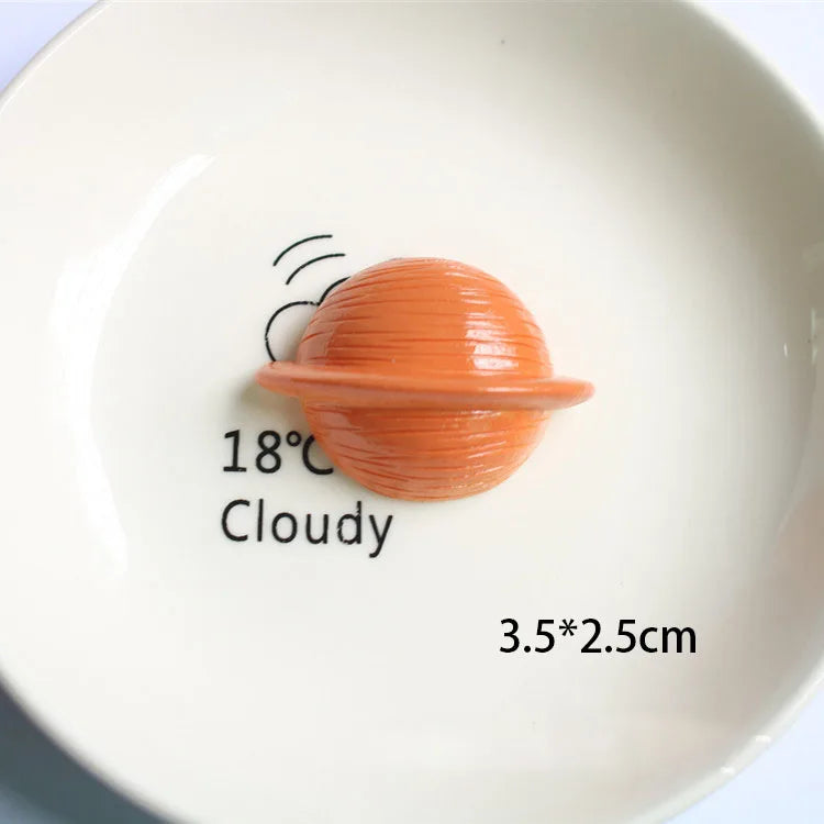 Une petite décoration de gâteau sphérique, orange, en forme d'astronaute, sur une assiette blanche.