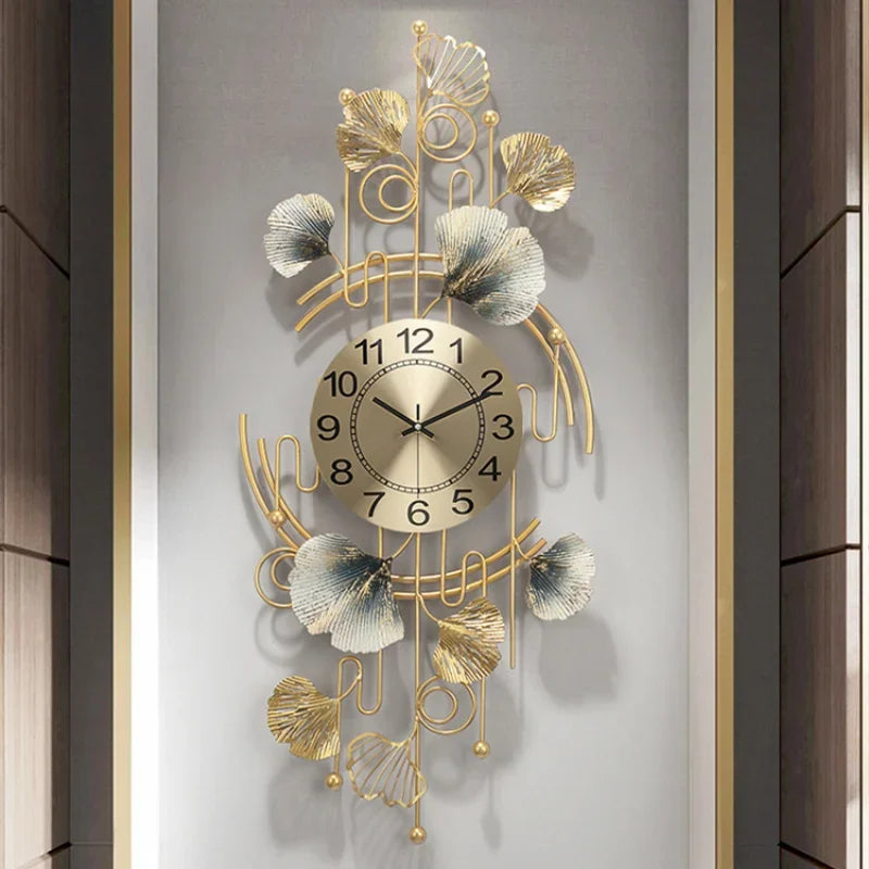 A vertical wall clock featuring a gold-toned metal design with leaf and floral elements, set against a light gray background.
