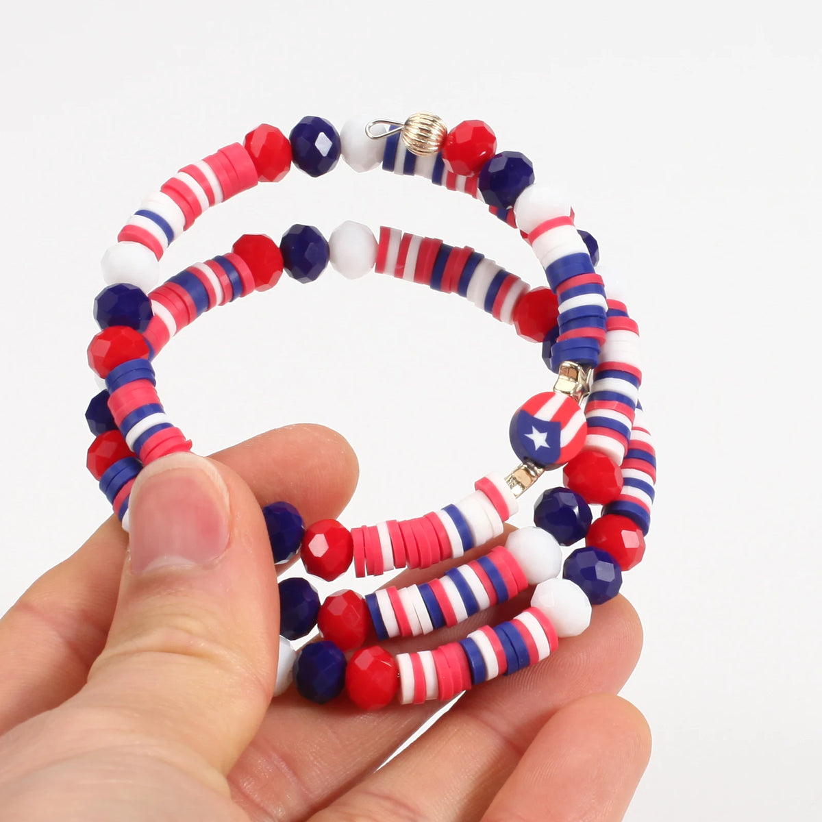 A hand holds a set of patriotic American flag beaded stretch bracelets featuring red, white, and blue beads.