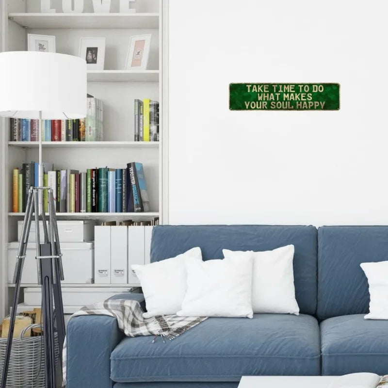 A vintage metal sign on a white wall reads Take time to do what makes your soul happy above a blue sofa.