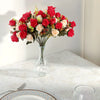A bouquet of realistic silk red and cream roses in a clear glass vase on a white tablecloth.