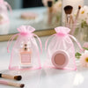Two pink organza drawstring bags containing a perfume bottle and a round cosmetic product are displayed on a white surface.