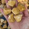 A hand holds several tumbled natural raw healing crystal stones in shades of yellow and amber.