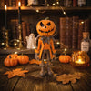 Figurine de citrouille orange déguisée en personnage effrayant, posée sur une surface en bois entourée de feuilles d'automne