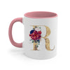 A pink ceramic coffee mug featuring a large gold letter R decorated with floral accents.
