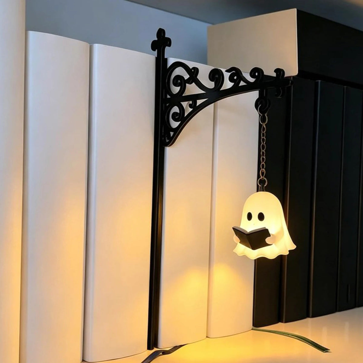 A black wrought iron lantern with a white ghost light hangs in front of a white vertical bookshelf.