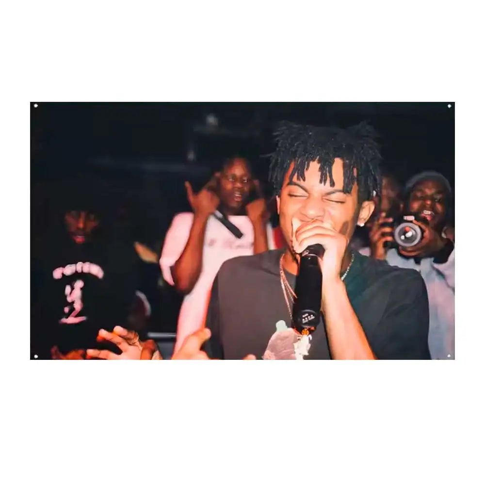 A close-up photo of a young man performing, holding a microphone on stage with other people in the background.