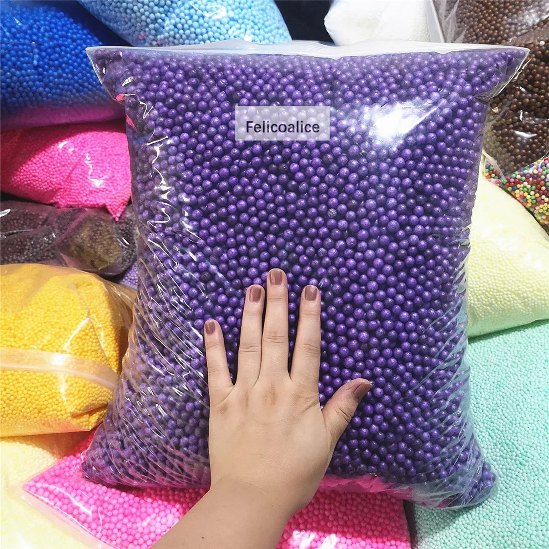 A hand is holding a purple bag filled with foam beads for crafting and decoration.