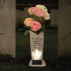 A stone vase holding pink and white roses with an LED light, placed in a cemetery setting.