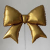 A golden foil balloon shaped like a bow, used for party decorations.