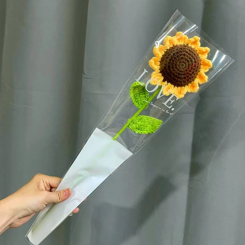 A clear plastic sleeve containing a handmade crochet sunflower bouquet with green leaves and the word LOVE written on it.