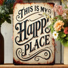 A rustic iron wall sign with carved text that reads This Is My Happy Place, displayed on a wooden shelf.