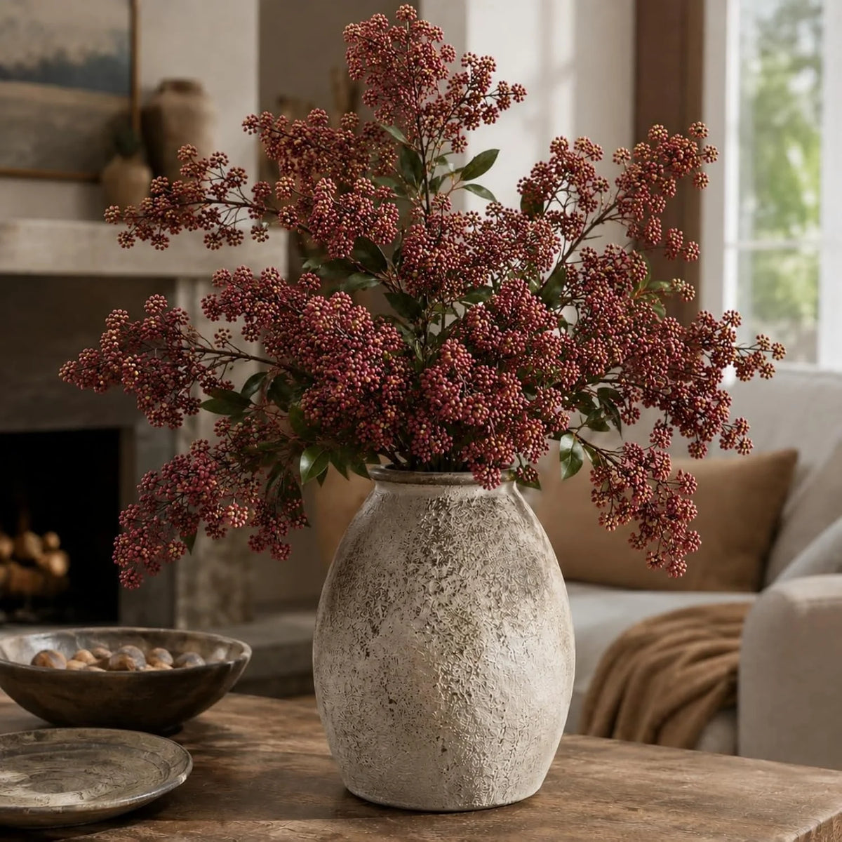 A faux branch of artificial nandina berry stem with dusty plum colored berries in a textured vase on a wooden table.