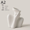 A white ceramic figural vase shaped like an artistic human form, shown from the side.